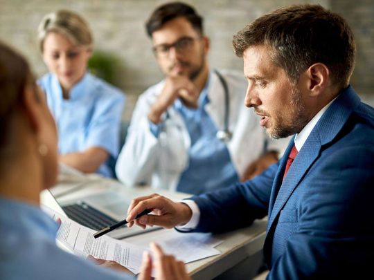 A man in a suit is sitting at a table talking to a group of doctors.