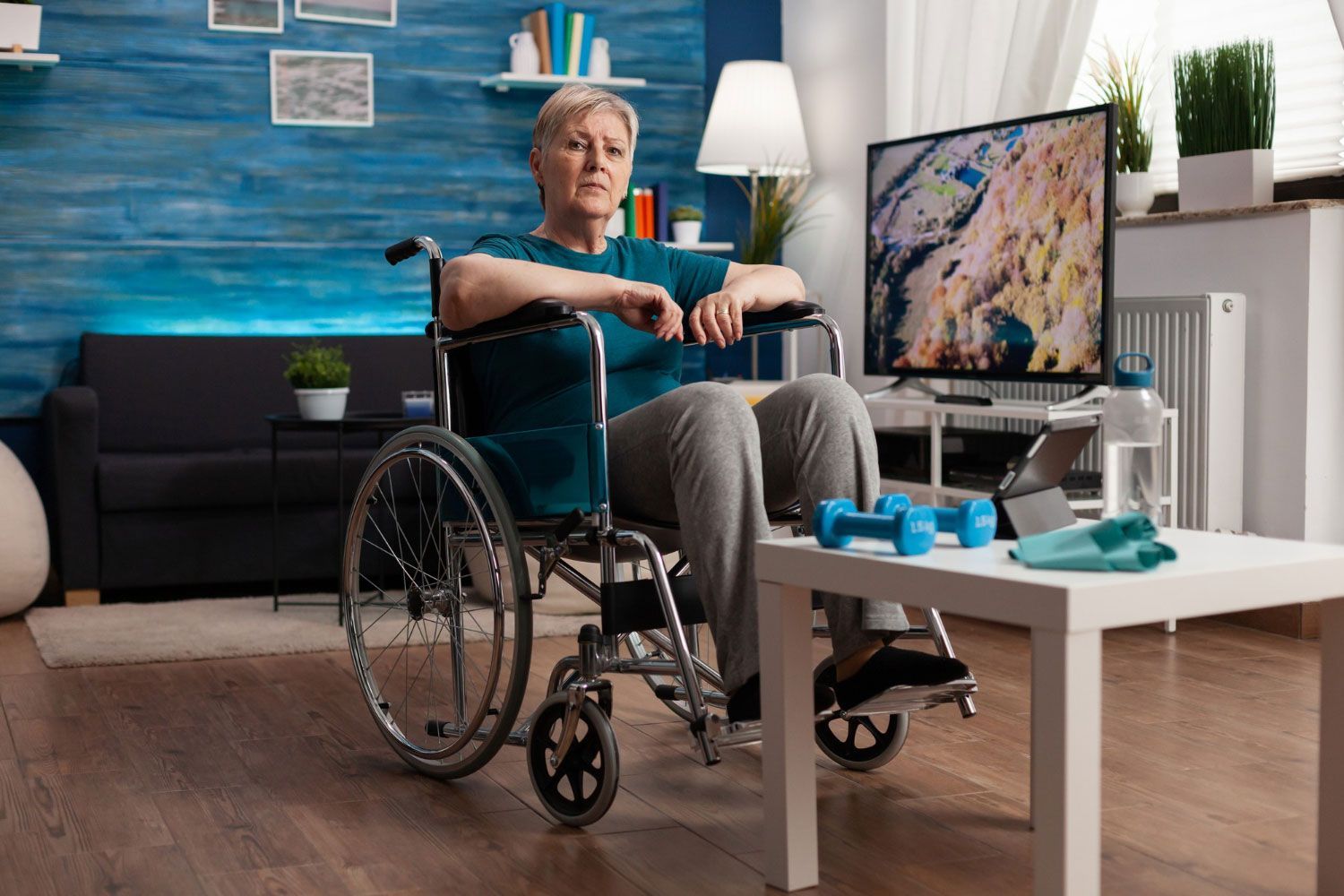 An elderly woman in a wheelchair is sitting on a table in a living room.