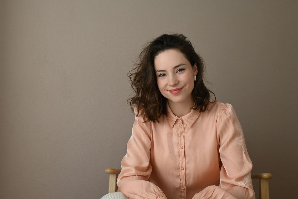 Vrouw in een perzikkleurige blouse lacht tegen een effen beige achtergrond.