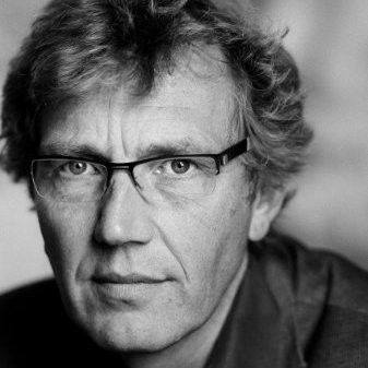Zwart-wit portret van een man met een bril, die recht in de camera kijkt.