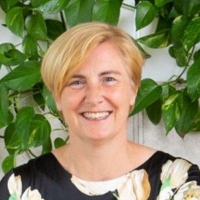 Lachende vrouw in een zwart-wit bloemenblouse voor groene, weelderige planten.