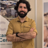 Een man staat met zijn armen over elkaar, gekleed in een mosterdkleurig shirt, voor een posterdisplay.