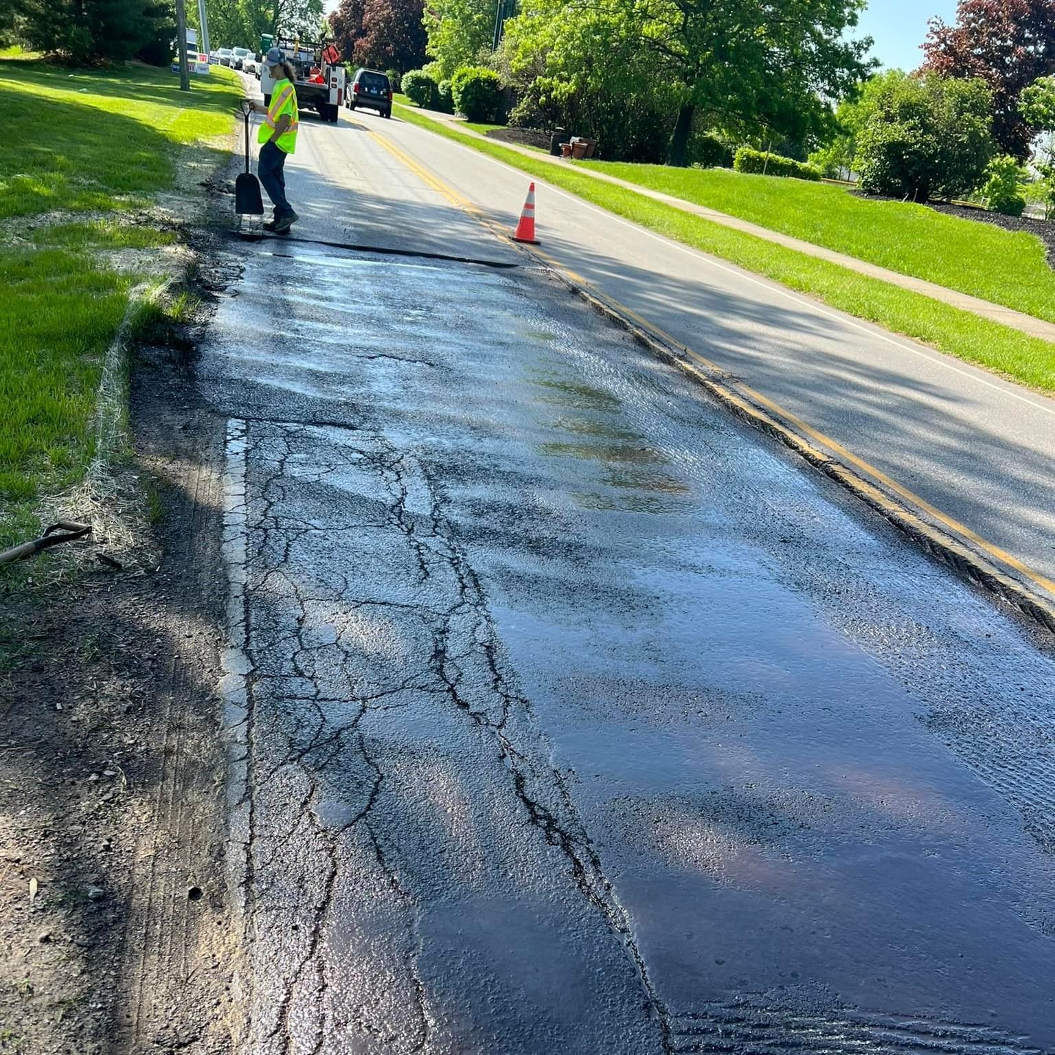 A man is standing on the side of a road with a shovel.