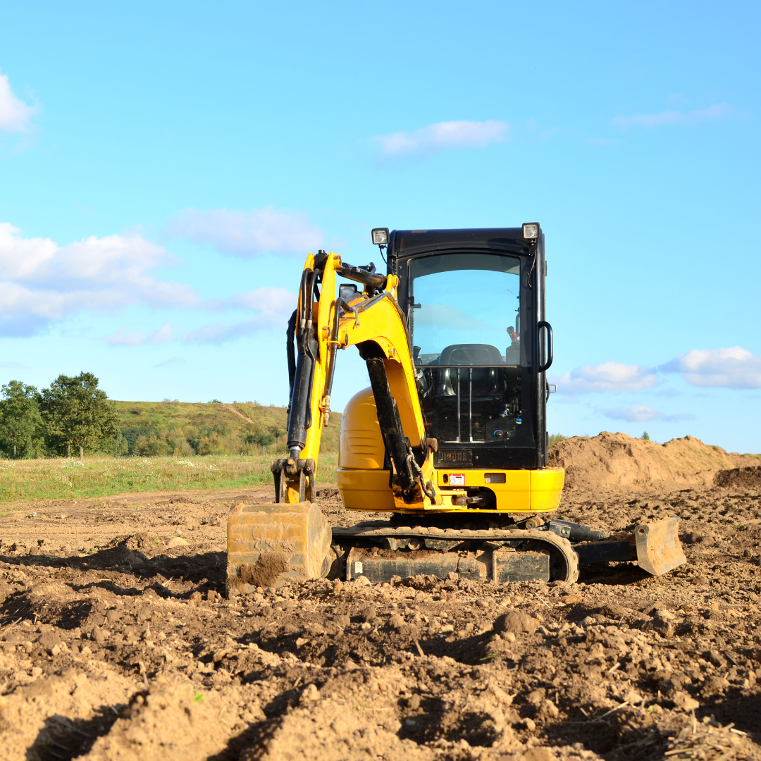 A yellow excavator is moving dirt in a field.