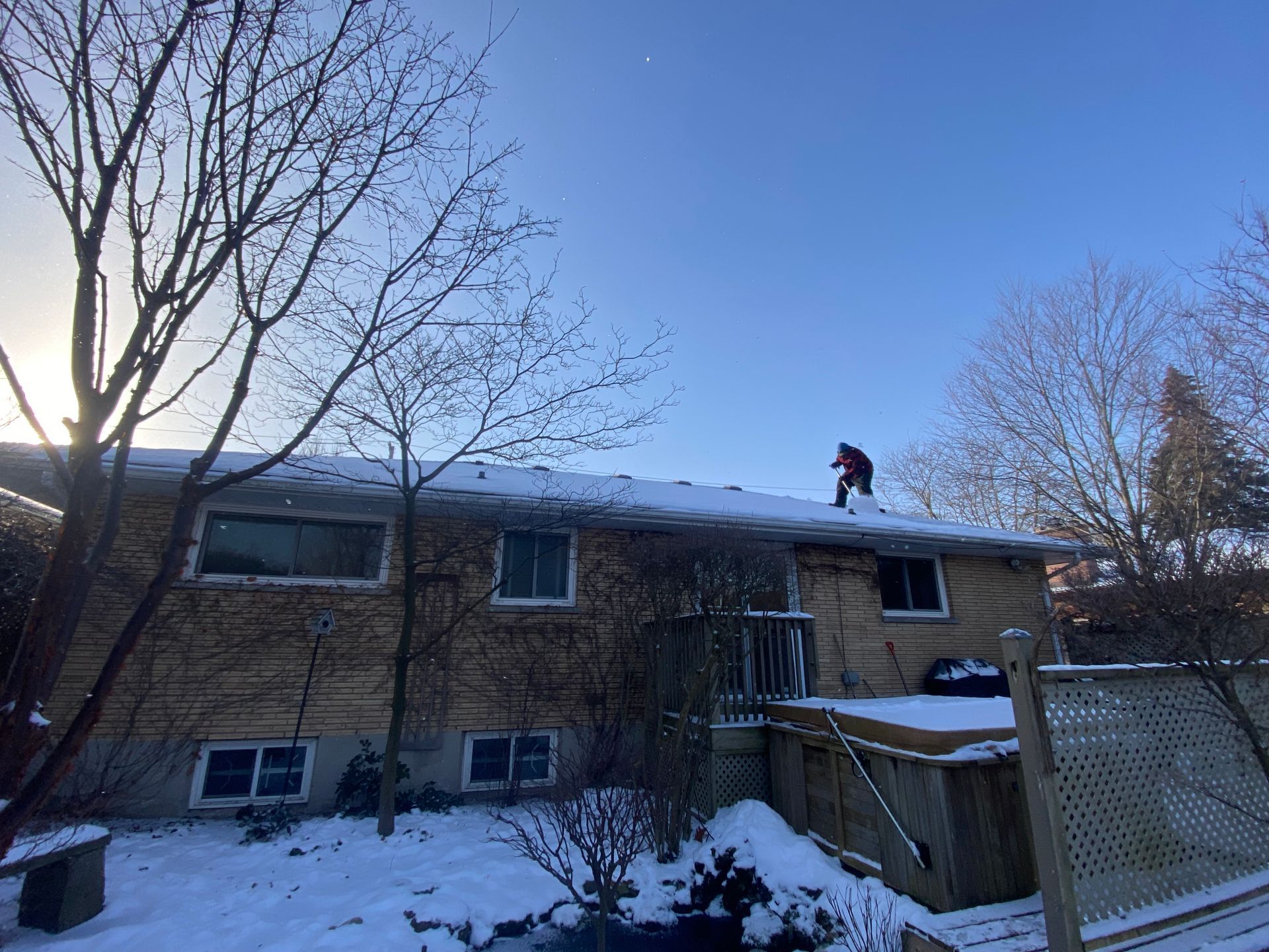 A man is standing on the roof of a house in the snow.