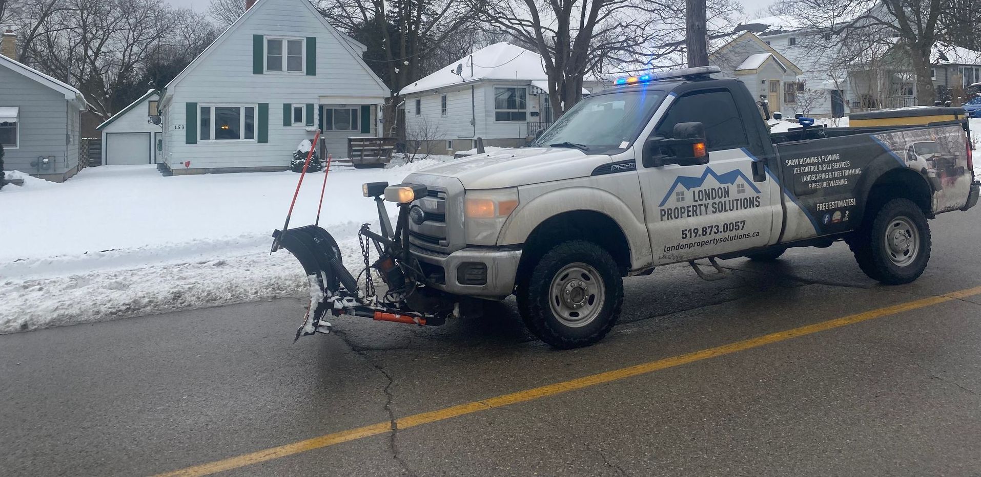 A white truck with a snow plow attached to it is parked on the side of the road.