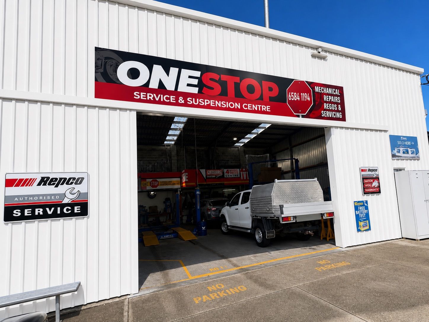 Auto repair shop exterior with open bay, parked vehicle inside, and “ONE STOP Service & Supplies Centre” sign