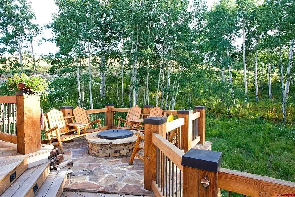 Wooden deck seating area with stone fire pit overlooking a grassy birch grove
