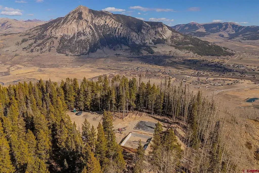 Aerial view of a forested valley with a small building amid trees and mountains under a clear sky