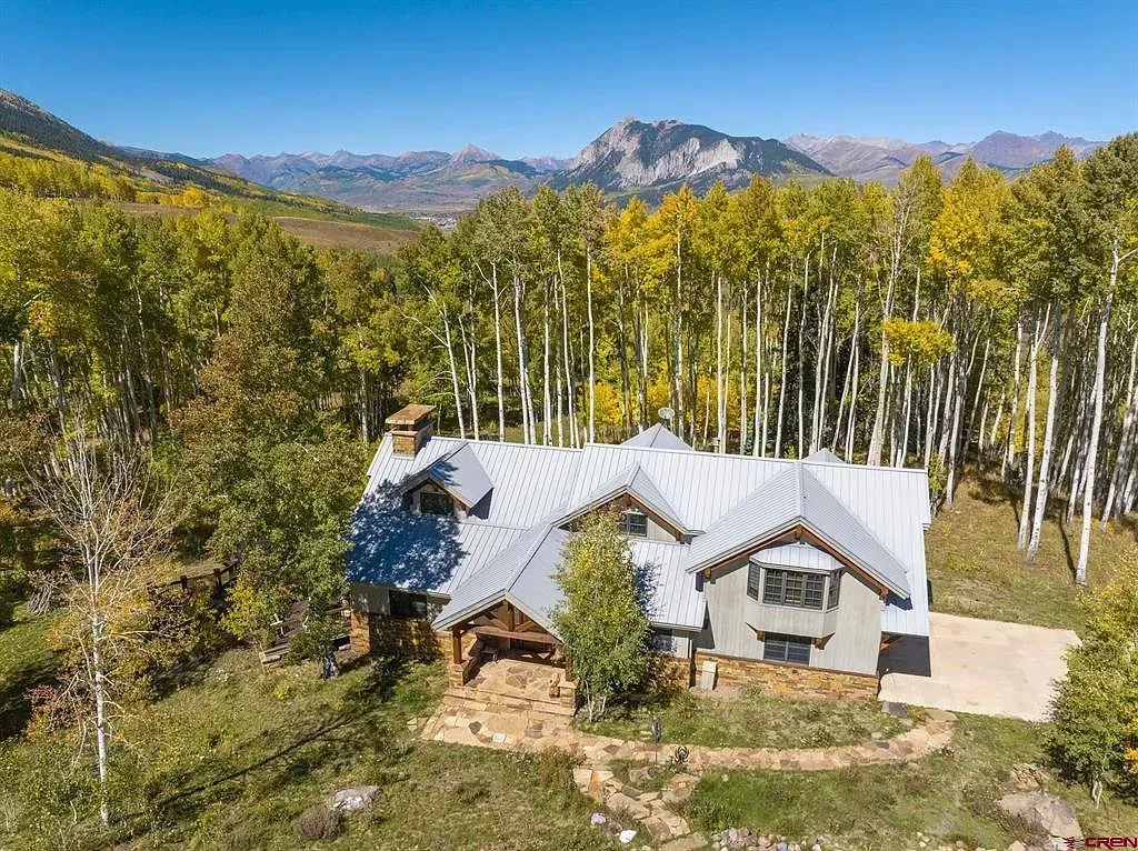 Rustic cabin with a white metal roof in a wooded mountain valley under a clear blue sky
