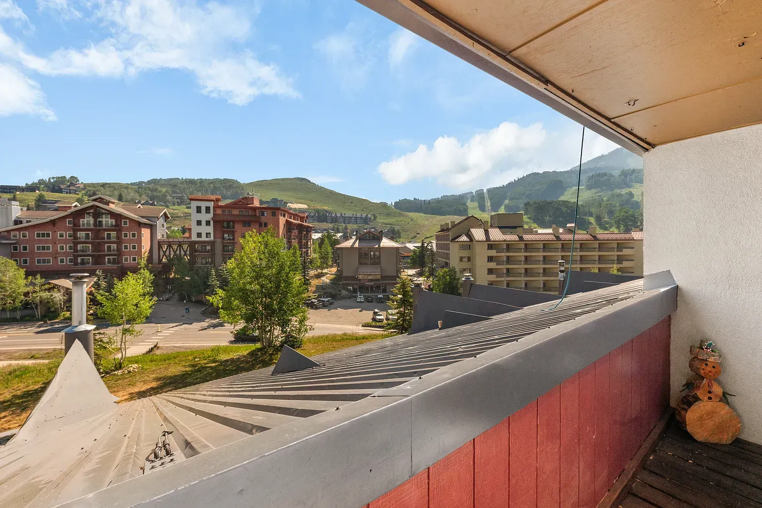 Balcony view of a mountain town with apartment buildings, trees, and blue sky