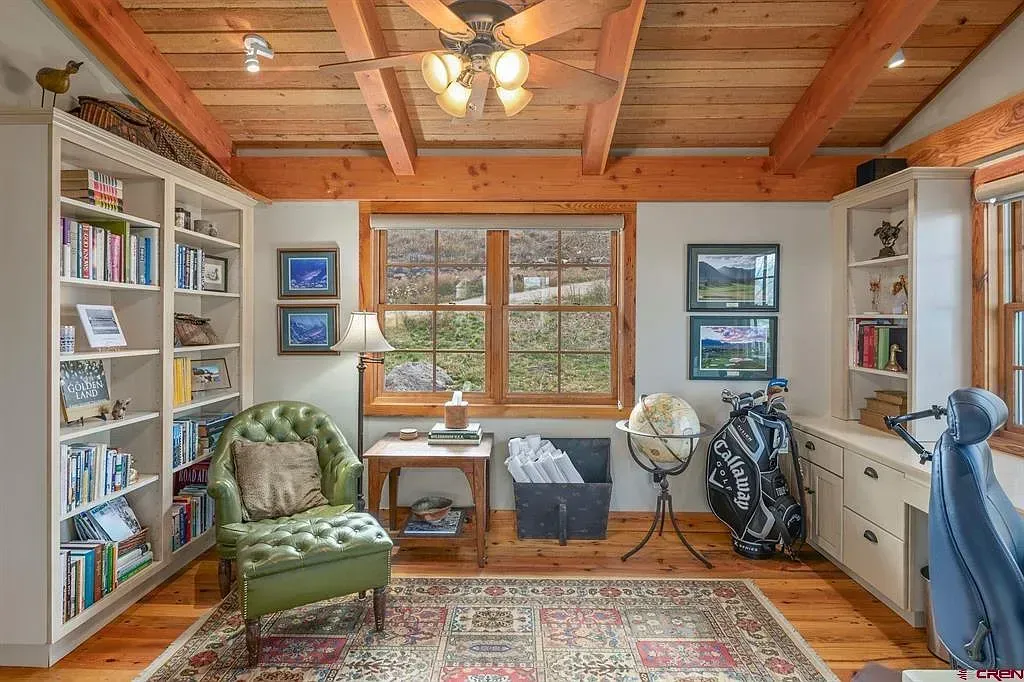 Cozy wood-paneled room with bookshelves, armchair, desk by window, globe, and patterned rug