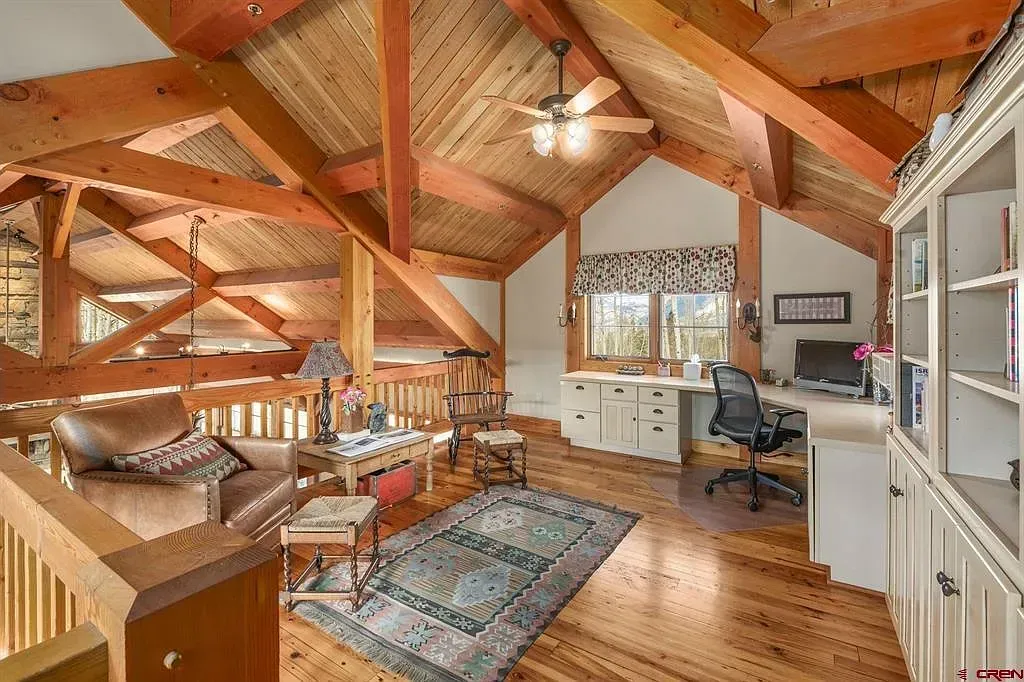 Cozy loft living room with wood beams, hardwood floors, a sofa, desk, and large windows