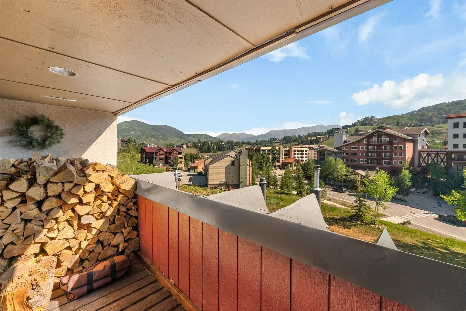 Balcony view of stacked firewood and red railing overlooking mountain village buildings and hills