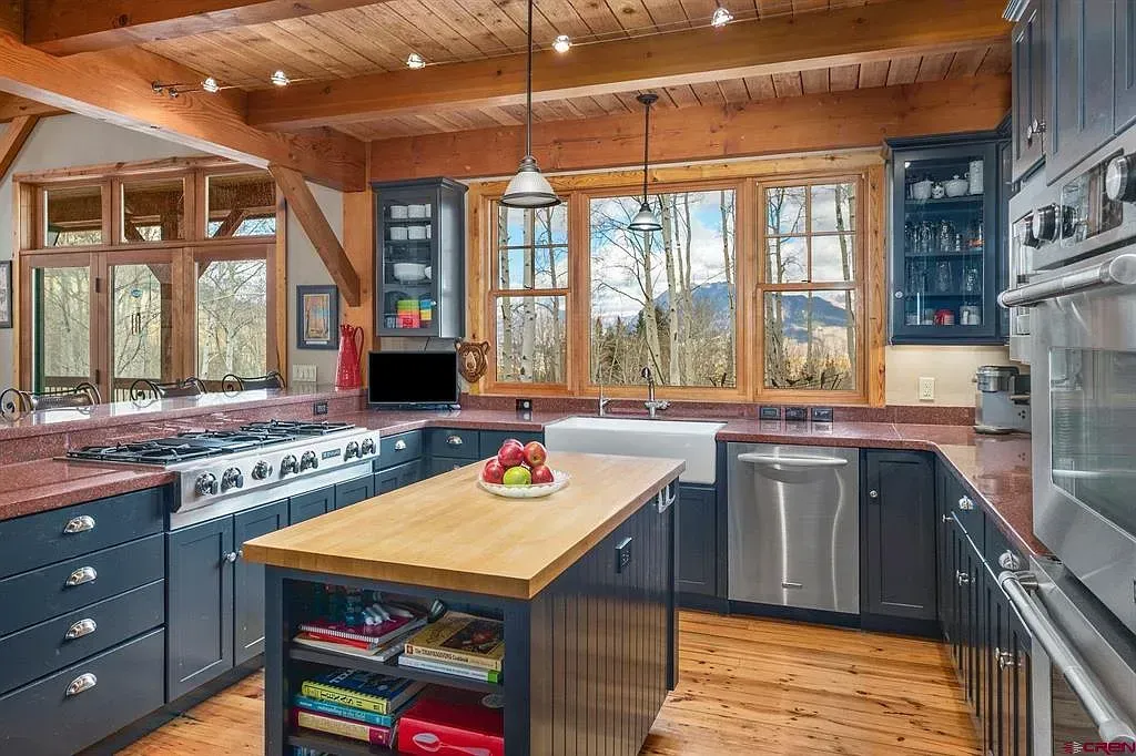 Rustic modern kitchen with wood ceiling, large windows, gray cabinets, and an island with fruit bowl
