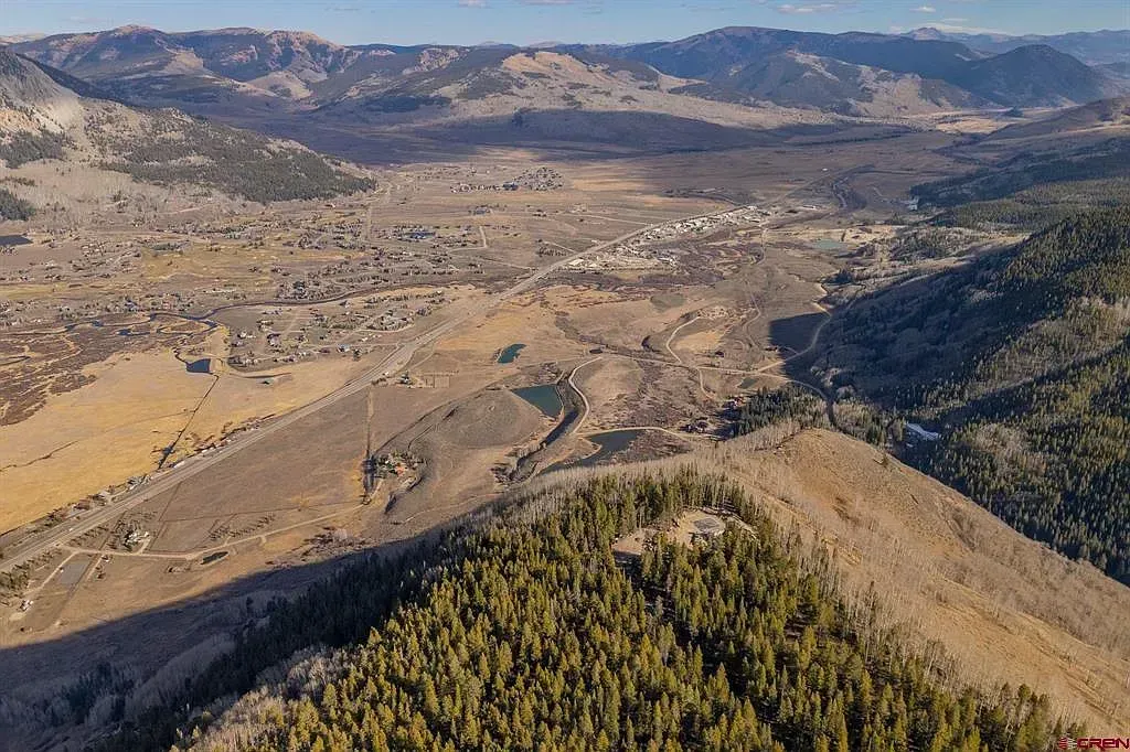 Aerial view of a mountain valley with evergreen forests, rocky hills, and a sunlit open plain