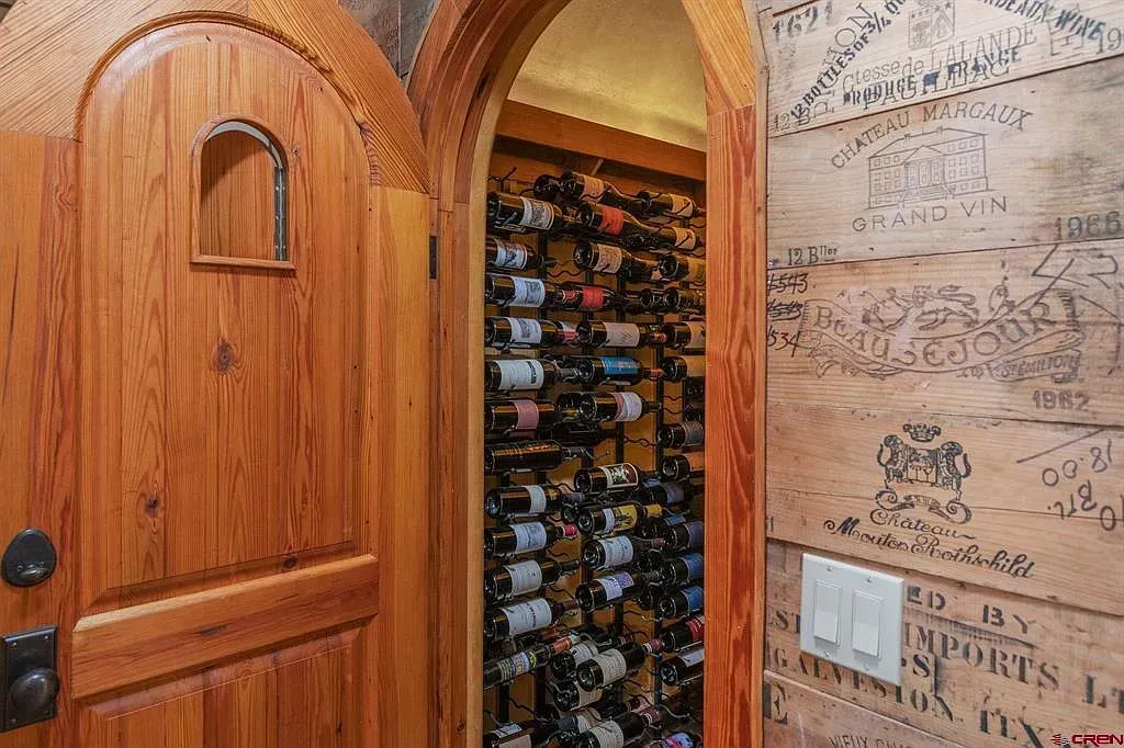 Wooden door opening to a wine rack closet, with the entry wall covered in handwritten signatures.