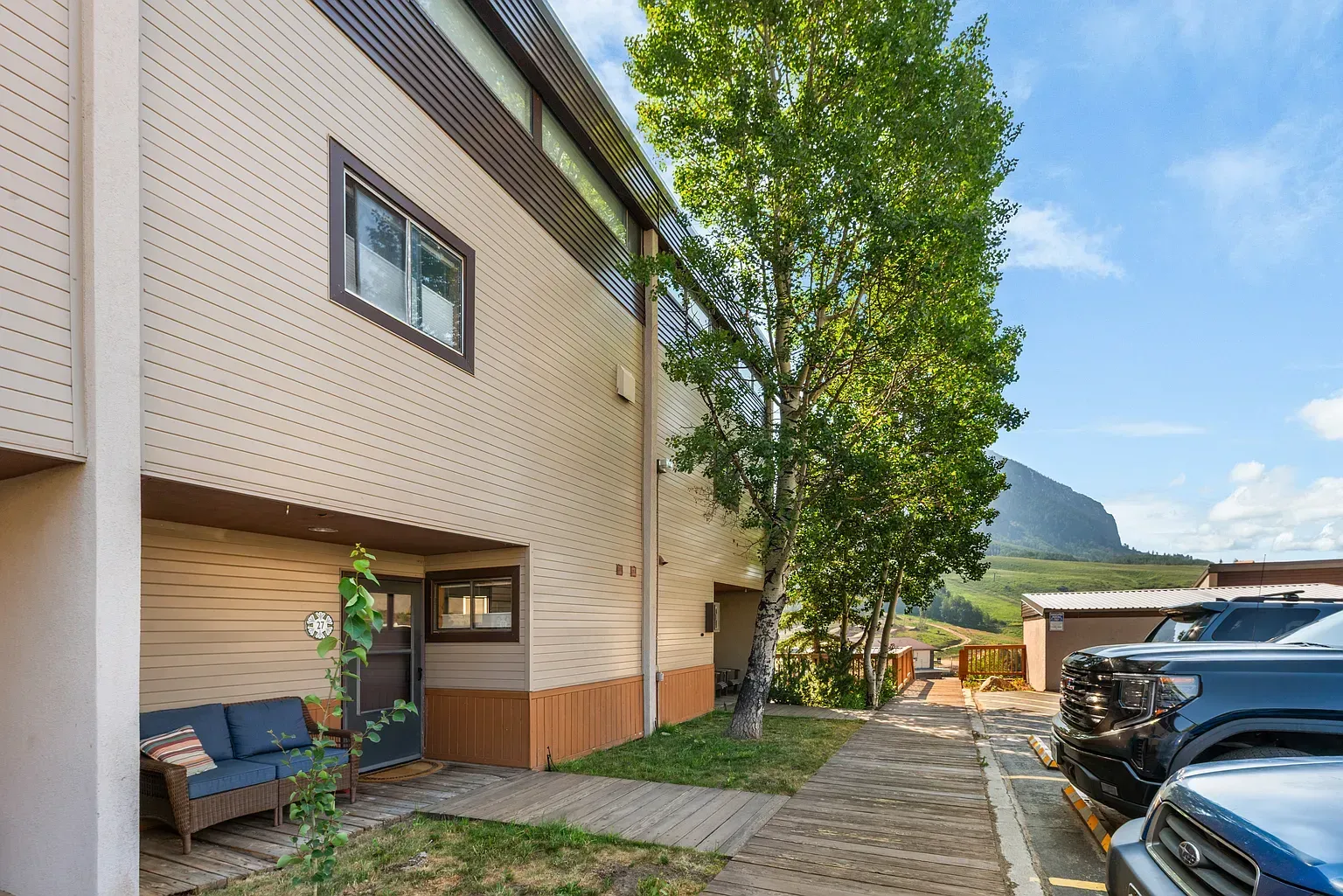 Apartment building exterior with parked cars, a tree, and a mountain in the background