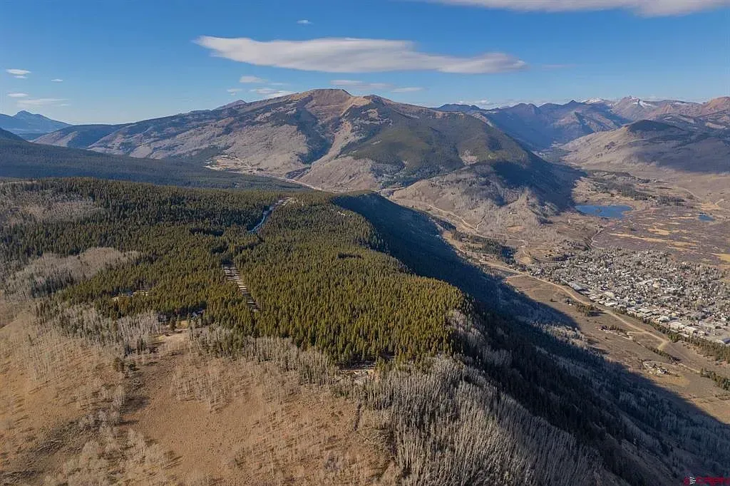 Aerial view of a forested mountain ridge under a blue sky with scattered clouds