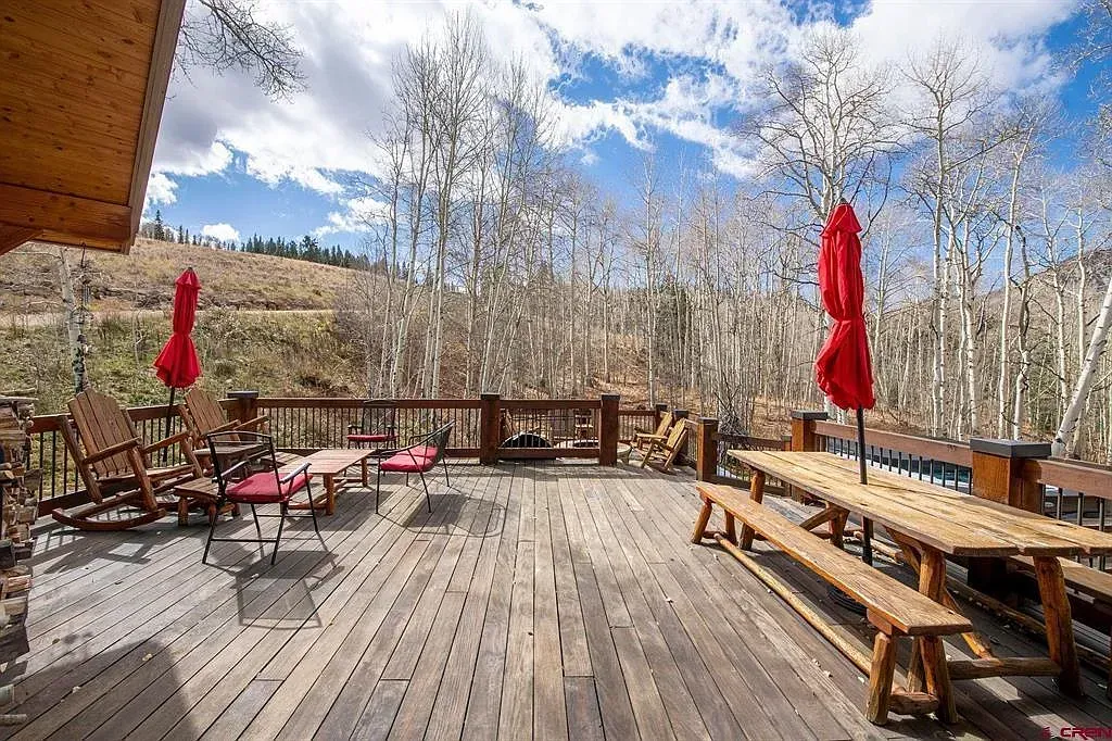 Wooden deck with red umbrellas, benches, and mountain views under a cloudy sky