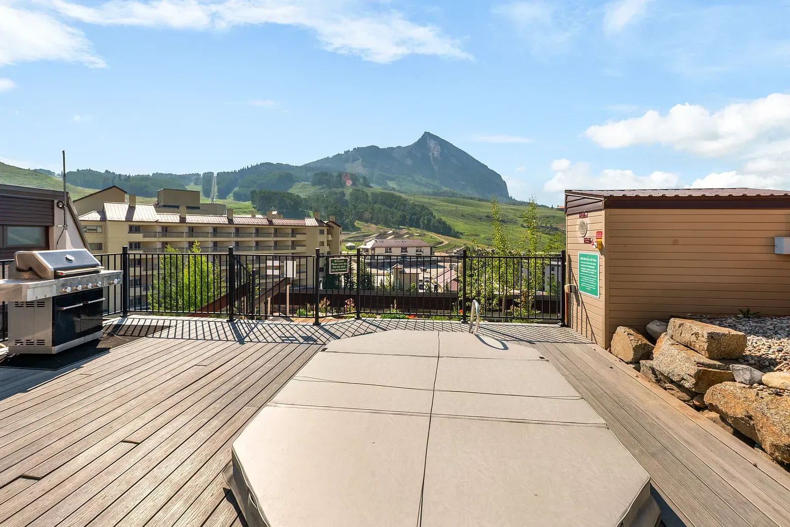 Mountain view from a rooftop deck with wooden benches and railings under a blue sky.