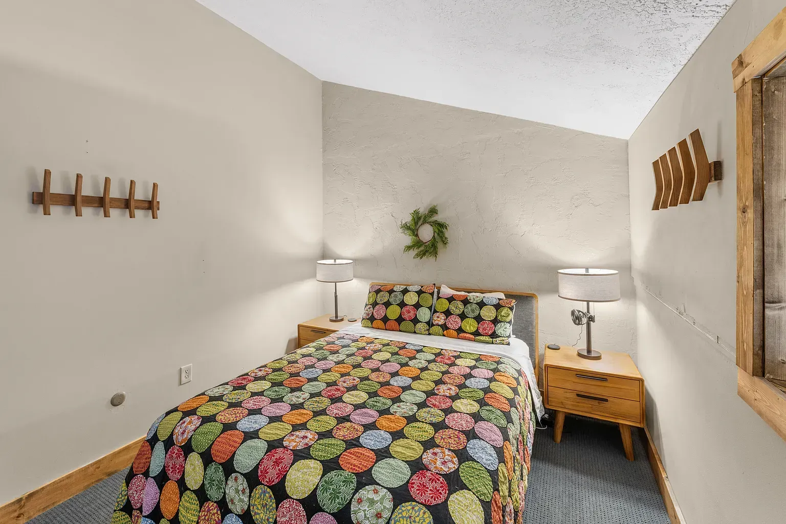 Cozy bedroom with colorful quilted bedspread, wood nightstand, wall decor, and neutral walls