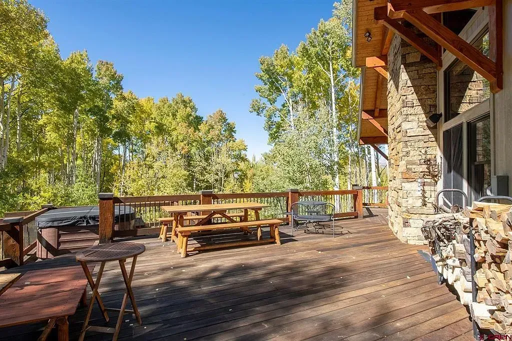 Outdoor wooden deck with picnic tables beside a rustic stone building and trees under a blue sky
