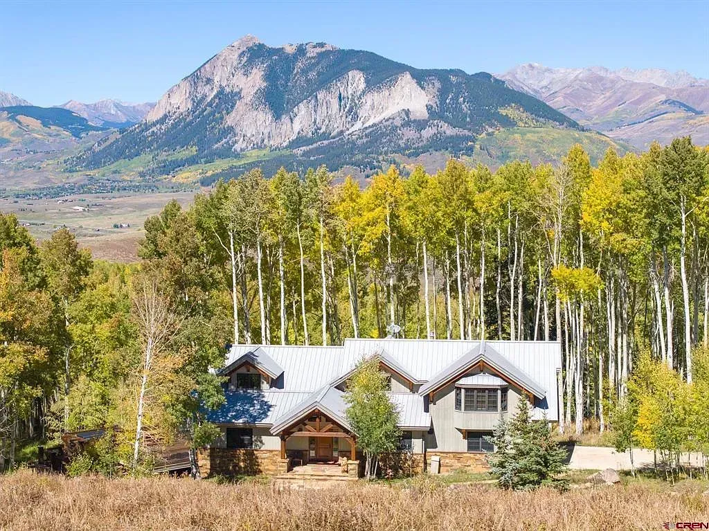 Mountain cabin with white roofs in front of yellow aspen trees and distant rocky peaks.