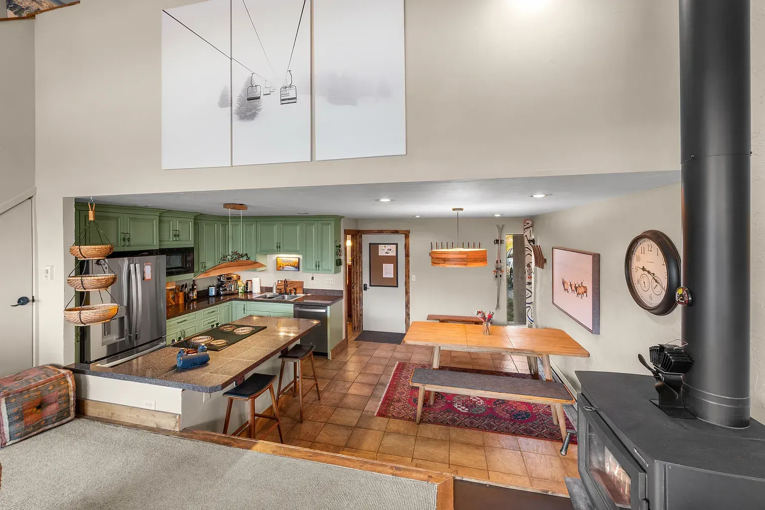Open-plan kitchen and dining area with green cabinets, wood floors, dining table, and wood stove