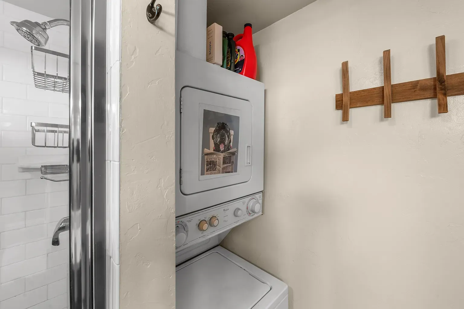Small laundry nook with stacked washer-dryer, shelves, and wall-mounted wooden rack