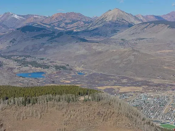 Mountain landscape with rocky peaks, a small blue lake, and a valley town below