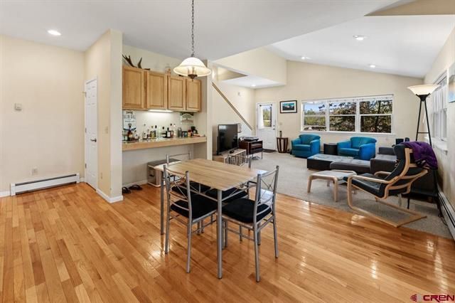 Bright open-concept living room and kitchen with hardwood floors, blue sofas, dining table, and large windows