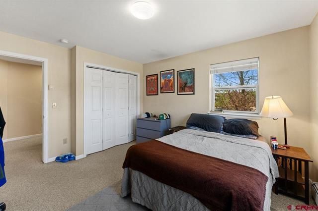 Bright bedroom with a made bed, bedside lamp, dresser, closet, and two windows.