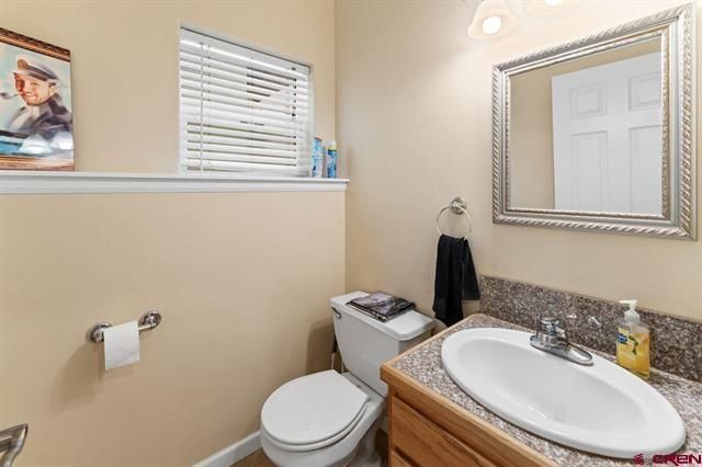 Small bathroom with toilet, sink, mirror, and window blinds
