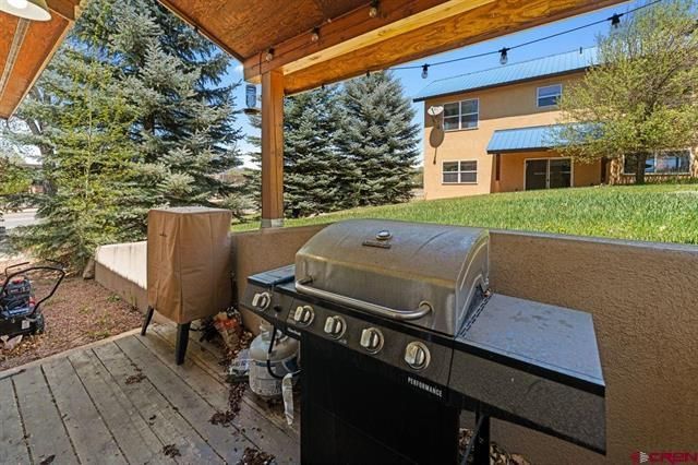 Covered patio with a gas grill, brown cabinet, and view of a grassy yard and house beyond.
