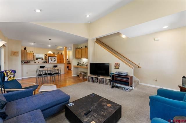 Bright living room with blue chairs, TV, staircase, and open kitchen in the background