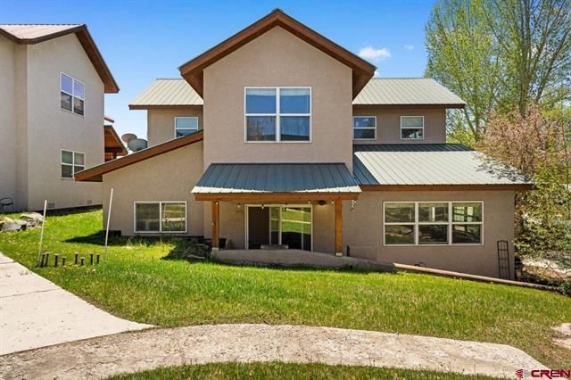 Two-story beige suburban house with brown roof, large windows, and a front lawn
