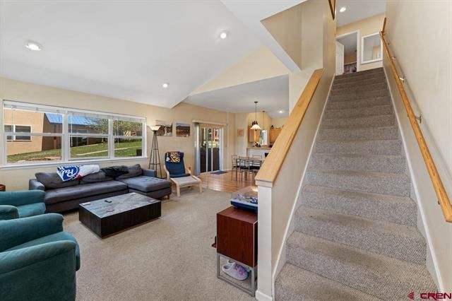 Bright living room with gray sectional sofa and carpeted staircase along the right wall.