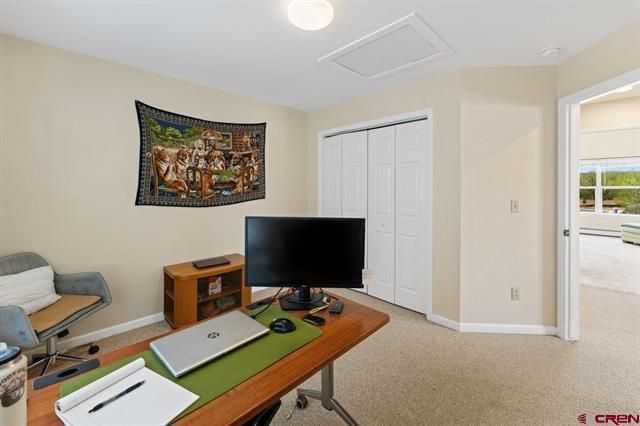 Home office with desk, monitor, chair, wall tapestry, and open doorway to a bright room