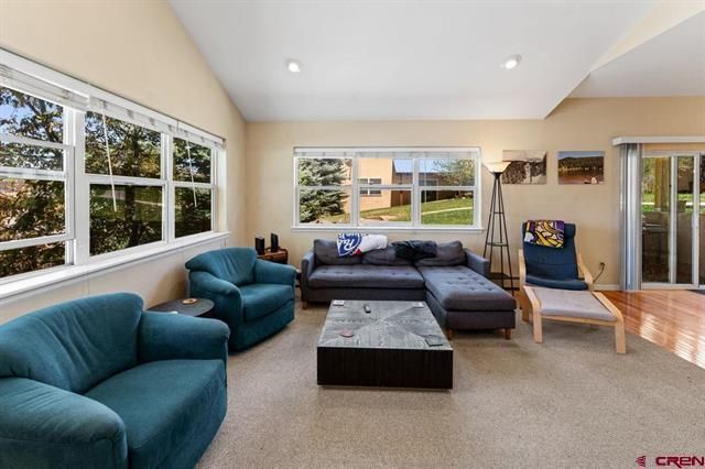 Bright living room with teal chairs, gray sectional, coffee table, and large windows.