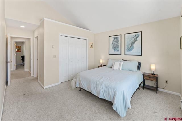 Bright bedroom with a bed, nightstands, framed art, and an open hallway view