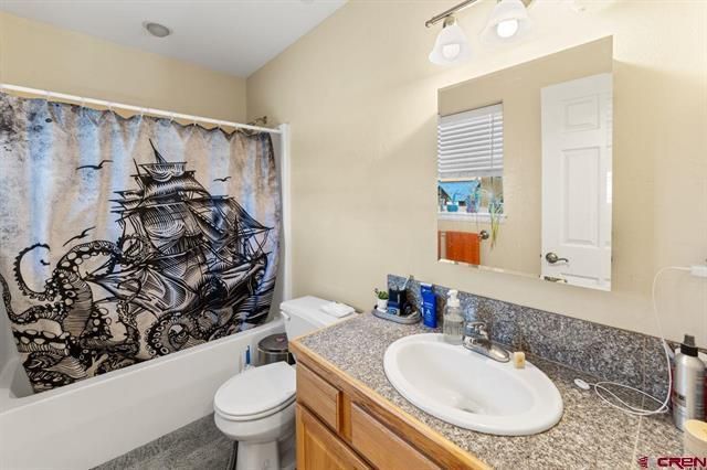 Bathroom with shower curtain, toilet, and vanity sink with granite countertop