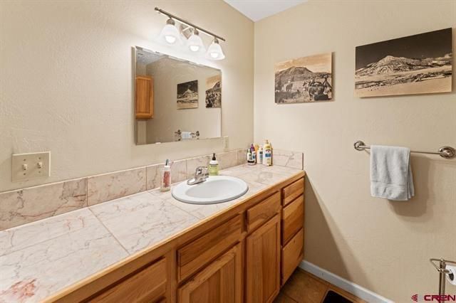 Bathroom vanity with wood cabinets, white sink, mirror, and wall art above a towel rack