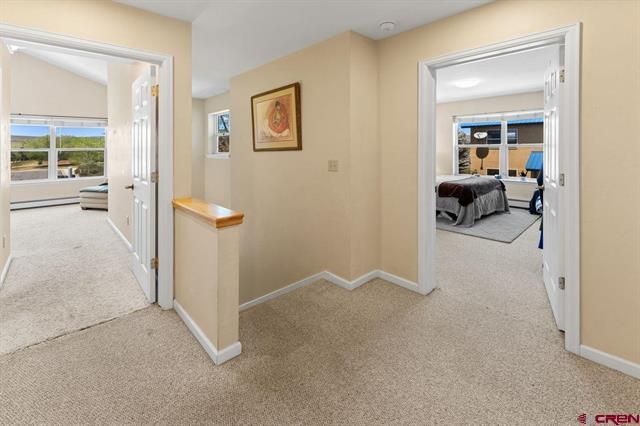 Bright hallway with beige carpet, white trim, and open doors to a bedroom and sunroom.