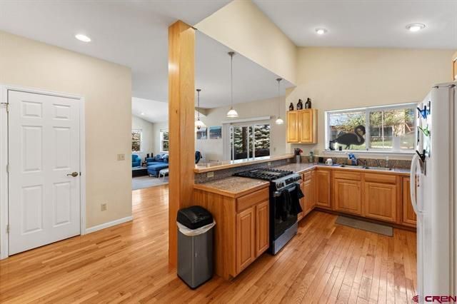 Bright kitchen with wood floors, oak cabinets, black stove, and a large mirror wall reflecting the room