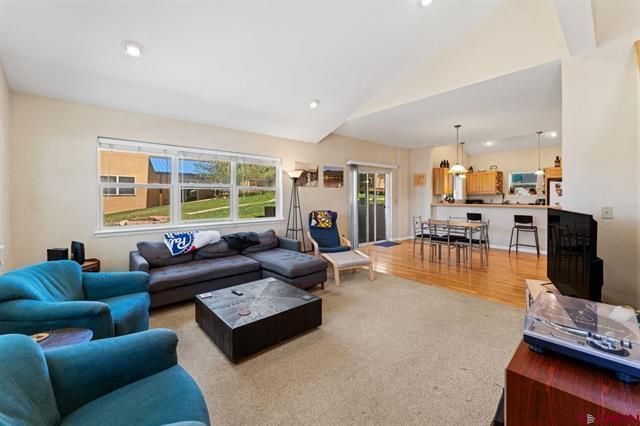 Bright living room with blue chairs, dark sofa, large windows, and open kitchen with bar stools.