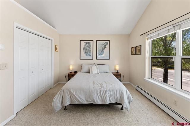 Bright bedroom with a neatly made bed, nightstands, closet doors, and large windows letting in daylight.