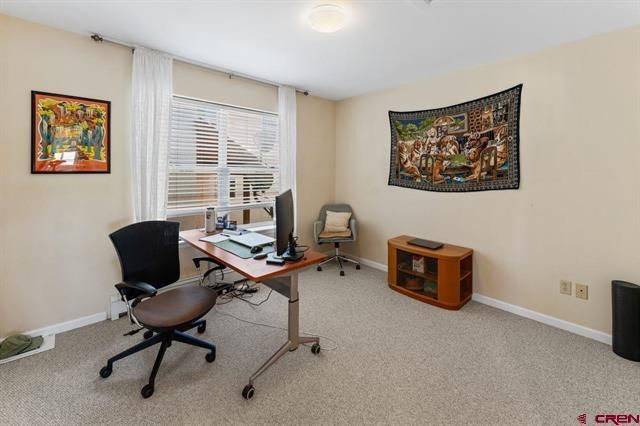 Home office with desk, computer, chair, window blinds, wall art, and a small TV stand on carpet.