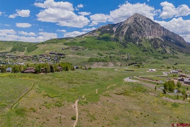 Wide green valley with a dirt path leading to a rocky mountain under a blue sky with clouds