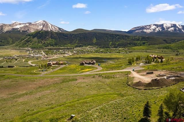 Green valley with winding roads, scattered buildings, and snow-capped mountains under a clear sky